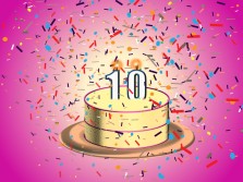 A yellow and pink birthday cake with lit #10 candles. The cake is showered in confetti.